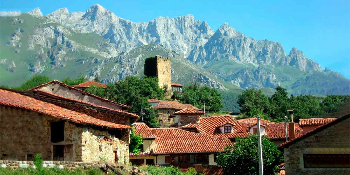 Vistas al centro histórico de Mogovrejo, uno de los pueblos bonitos de Cantabria, en el que se ve la torre antigua del pueblo y unas montañas enormes por detrás