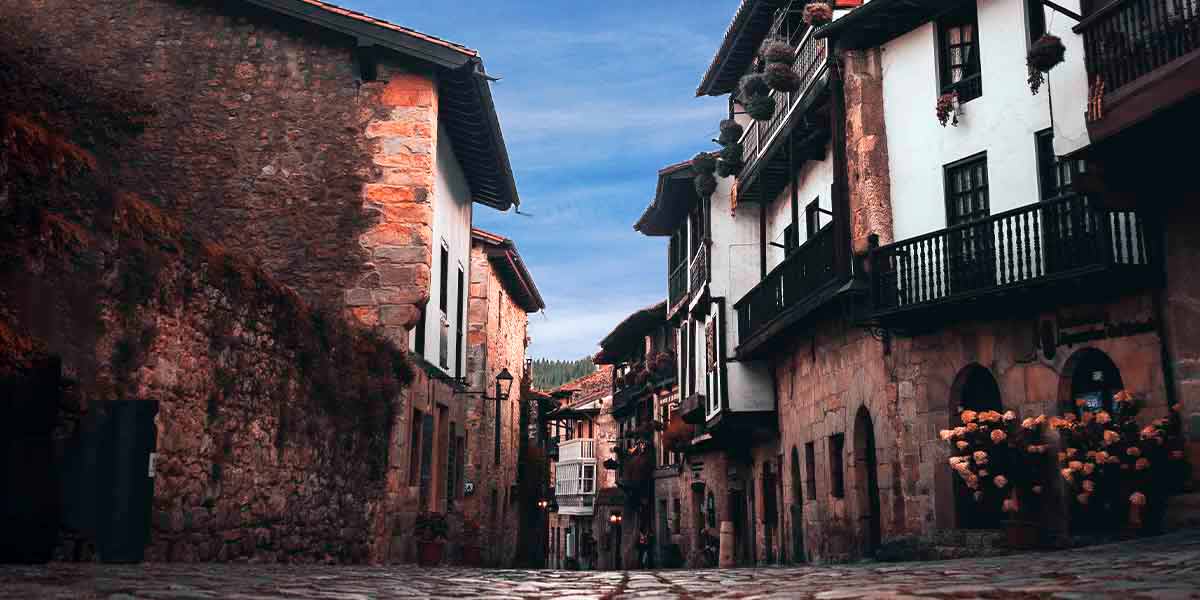 Una calle céntrica de Santillana del Mar en Cantabria, donde hay casas tradicionales decoradas con flores bonitas y el cielo azul