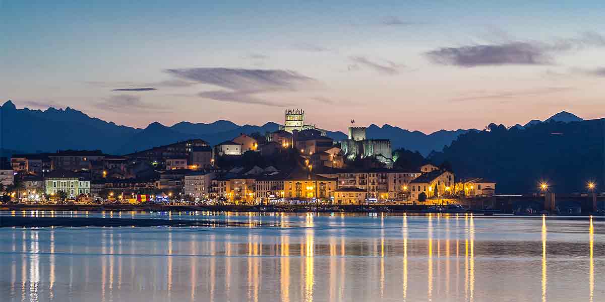 San Vicente de la Barquera por la noche con las luces encendidas y reflejadas en el agua del mar con las montañas de fondo