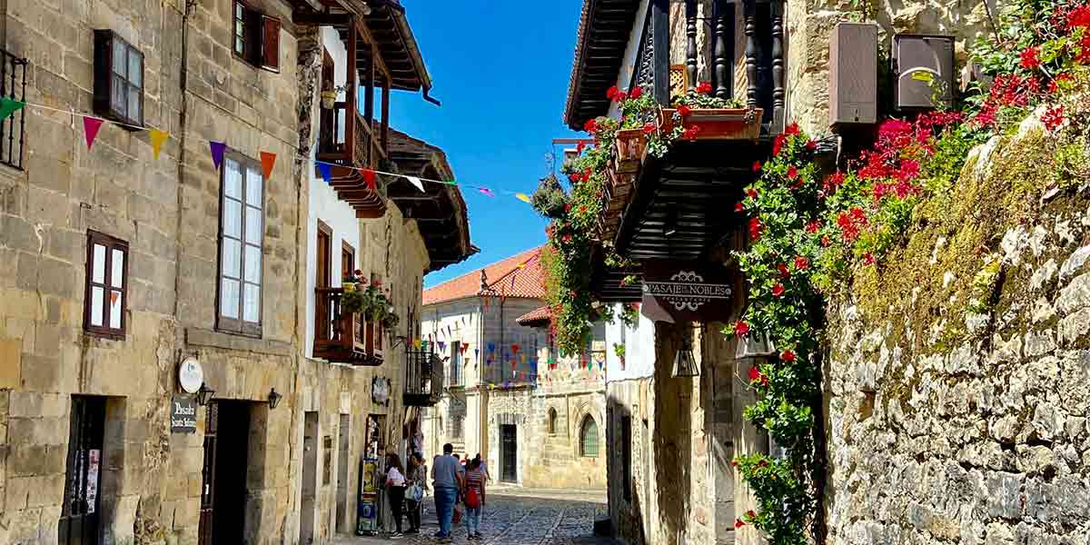  Santillana del Mar donde se ve una bonita calle del centro histórico, decorada con motivos festivos y repleta de flores