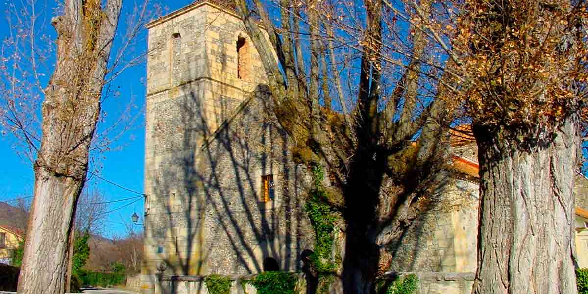 La histórica Iglesia Parroquial de Santa Marina Virgen y Mártir en Alameda del Valle construida con antiguas piedras y rodeada de robustos árboles