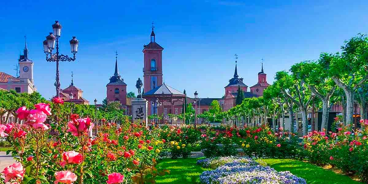 La pintoresca Plaza de Cervantes en Alcalá de Henares, repleta de flores coloridas, con la estatua de Cervantes y el Quiosco de la Música