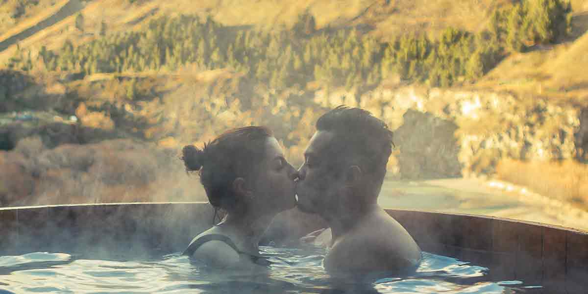 Una pareja enamorada dándose un beso sumergidos en el humeante agua de un jacuzzi exterior