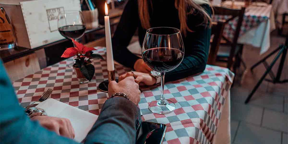 Una pareja teniendo una cita de cena romántica en el Barrio de las Letras, mientras se dan la mano y comparten una botella de vino, uno de los planes en pareja Madrid más románticos