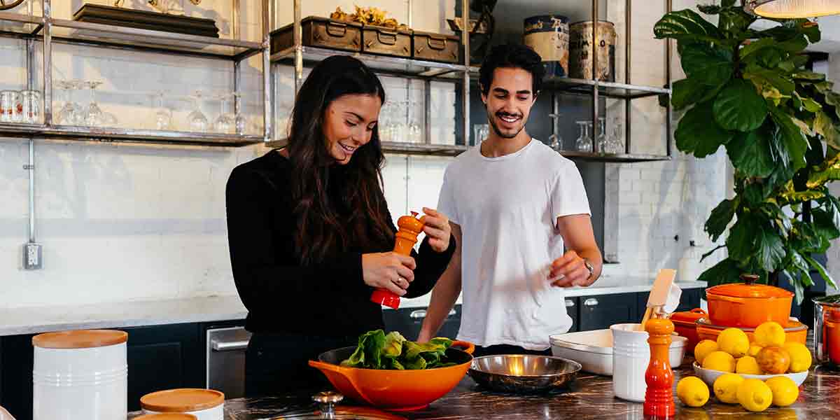 Una pareja pasándolo genial en una clase de cocina, donde preparan la comida y luego se la disfrutan juntos, uno de los planes en pareja Madrid más divertidos