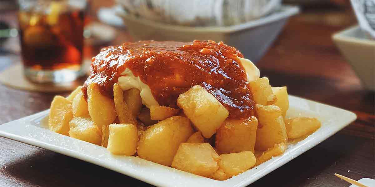 Una pareja haciendo un tour de tapas en un mercado tradicional en Madrid, donde se comen unas deliciosas patatas bravas