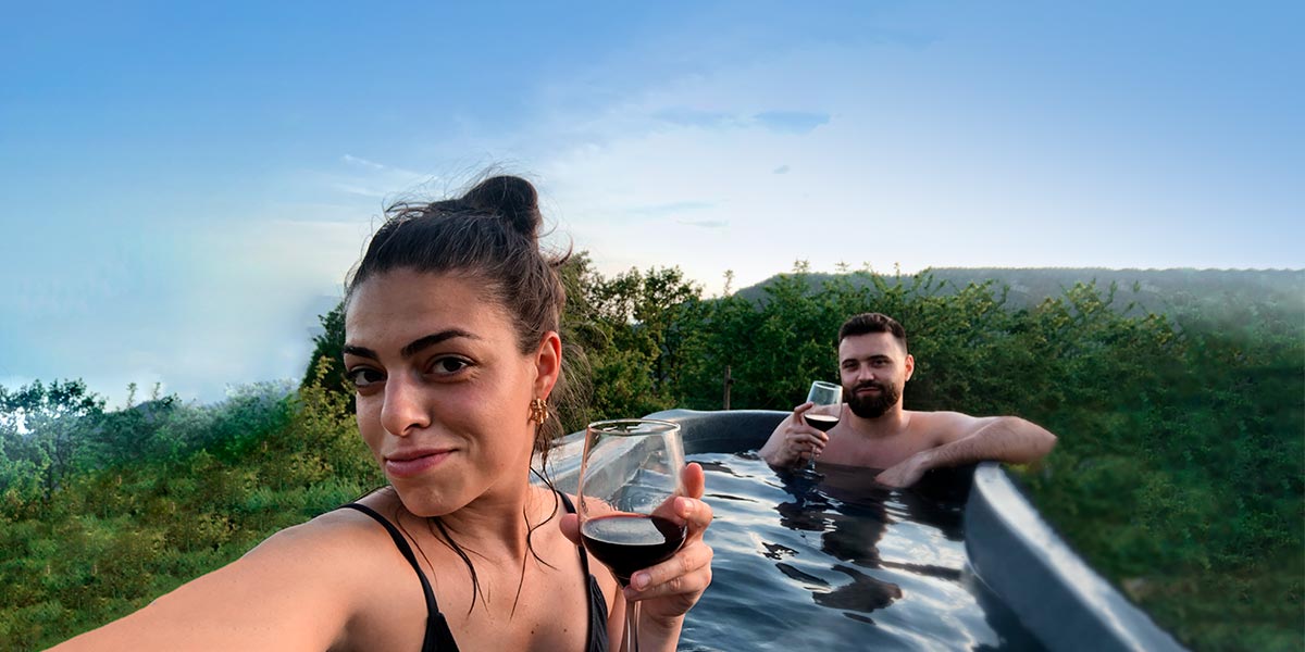 Una pareja en el jacuzzi de un glamping con cabañas en el bosque, considerado uno de los regalos para parejas más originales